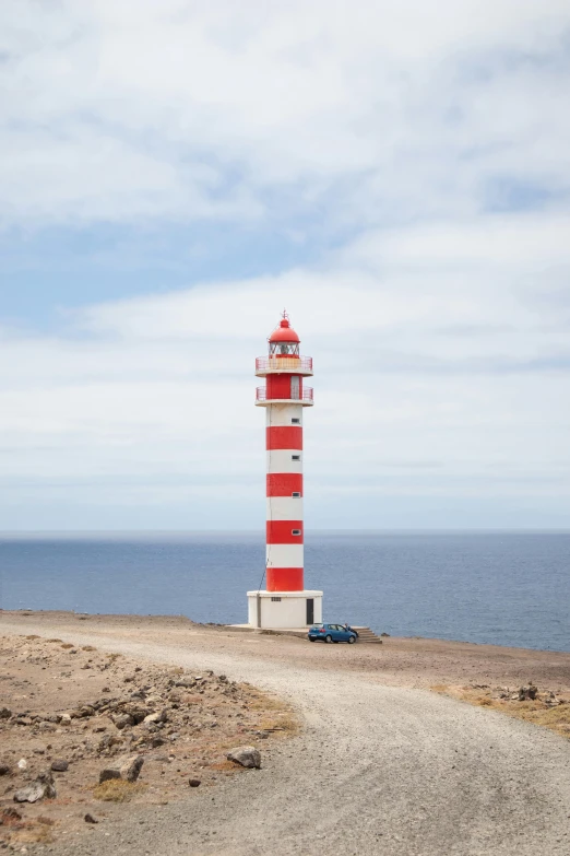 a red and white lighthouse sitting on top of a sandy beach, road, square, balaskas, high-quality photo