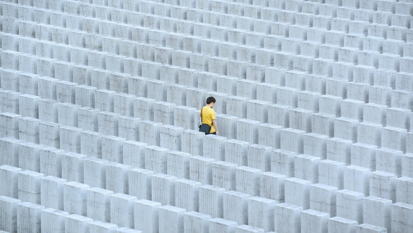 a person standing in a maze of concrete blocks, inspired by Andreas Gursky, minimalism, with yellow cloths, statue of angela merkel, giant grave structures, dezeen