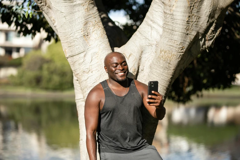 a man standing next to a tree holding a cell phone, huell babineaux, profile image, lean man with light tan skin, working out