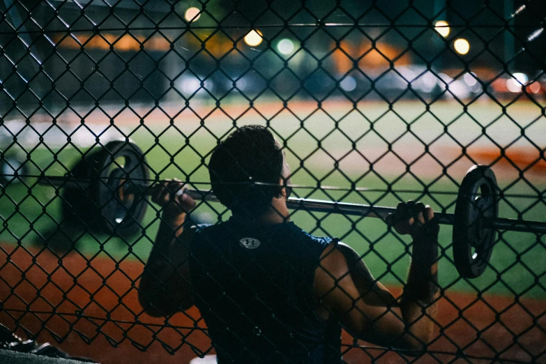 a man holding a barbell on top of a baseball field, cage, instagram picture, low lighting, profile image