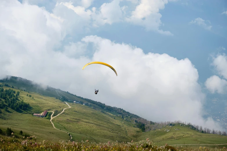 a person flying a kite on top of a lush green hillside, by Peter Churcher, pexels contest winner, hurufiyya, 9 9 designs, parachutes, bhutan, cafe in the clouds