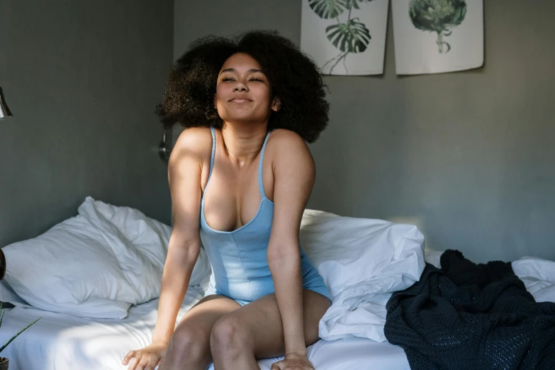 a beautiful young woman sitting on top of a bed, pexels contest winner, happening, cute girl wearing tank suit, with afro, soft grey and blue natural light, blue undergarments