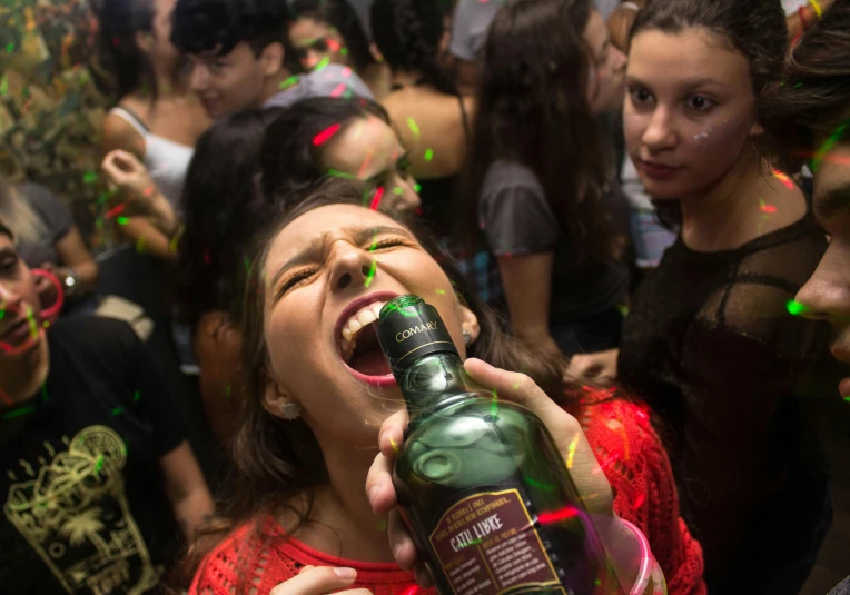 a woman holding a bottle of alcohol in front of a crowd of people, pexels, hyperrealism, headbanging, sao paulo, high school girls, profile image