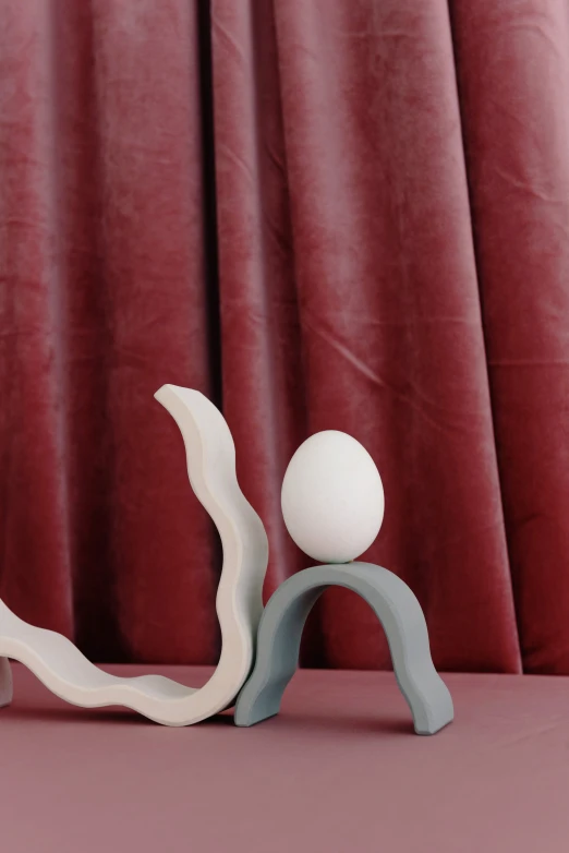 a couple of figurines sitting on top of a table, an abstract sculpture, inspired by Jean Arp, trending on unsplash, eggs, soft grey and red natural light, pastelwave, close-up on legs