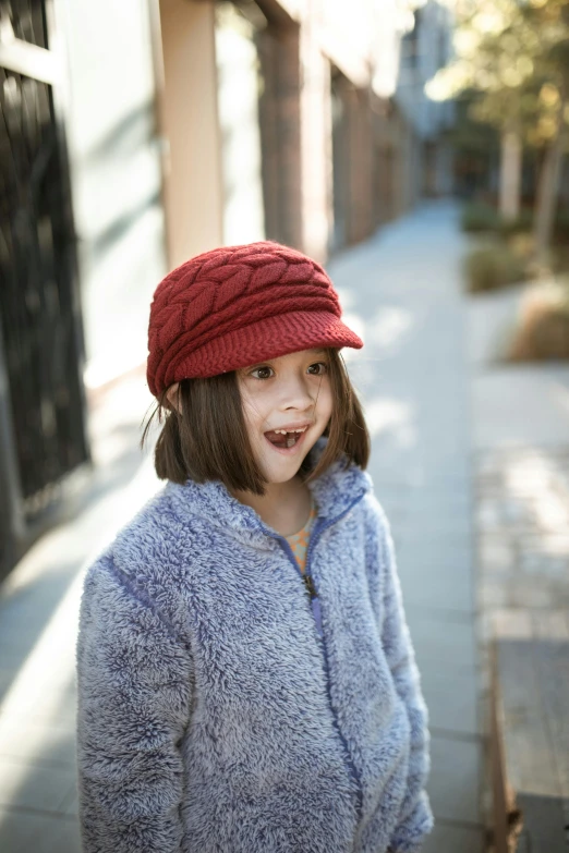 a little girl standing on a sidewalk wearing a red hat, official product photo, dolman, cozy warm tint, medium head to shoulder shot