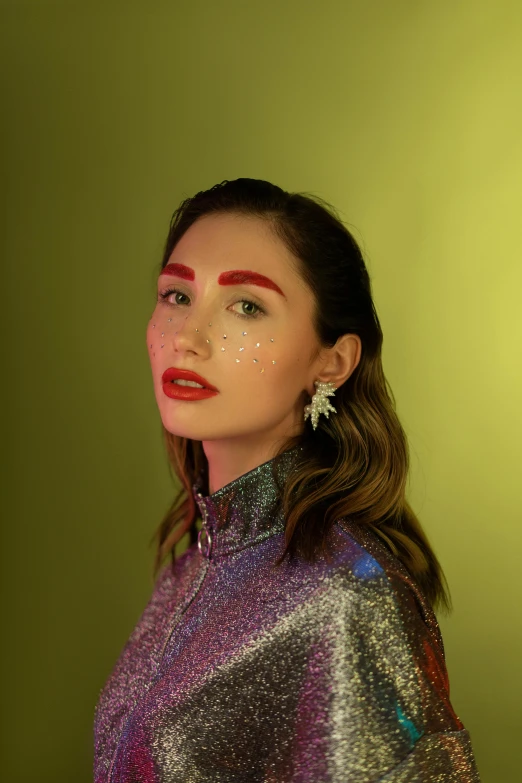 a woman standing in front of a green wall, an album cover, inspired by Julia Pishtar, trending on pexels, holography, big eyebrows, glitter makeup, wanda maximoff, ana de armas portrait