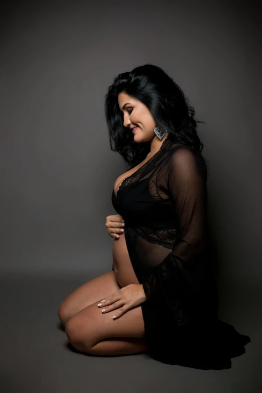 a woman sitting on the ground in a black dress, pregnant belly, very sexy woman with black hair, promo image, sheer