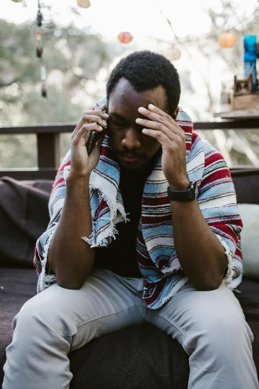 a man sitting on a couch talking on a cell phone, pexels, stressed and burnt out, man is with black skin, outside, scruffy man