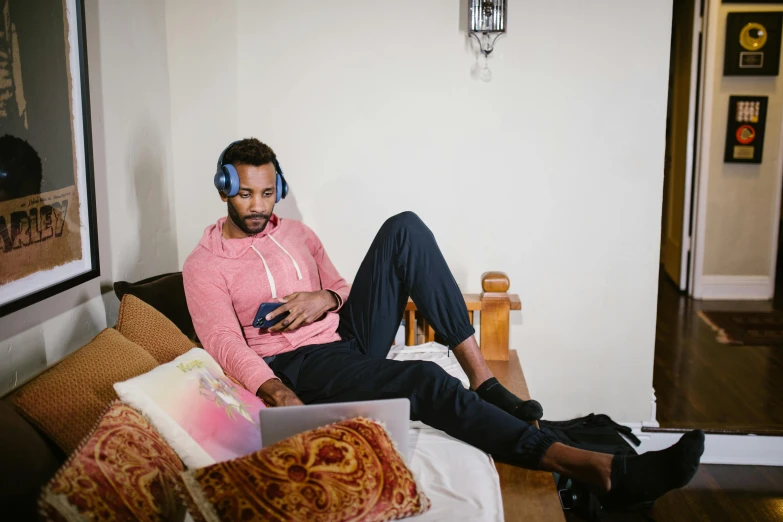 a man sitting on a couch with a laptop and headphones, by Carey Morris, trending on pexels, happening, brown skin man egyptian prince, a wide shot, wearing pajamas, a high angle shot