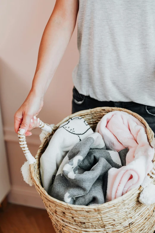 a woman holding a basket full of clothes, by Lucette Barker, pexels contest winner, pink and grey muted colors, adorable design, family friendly, detail shot