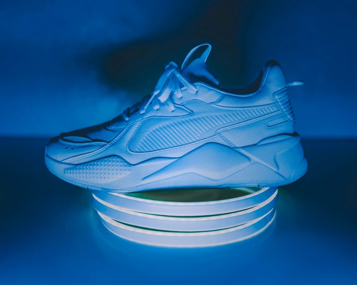 a pair of white sneakers sitting on top of a table, an ambient occlusion render, pexels contest winner, holography, dramatic blue lighting, based on a puma, ring lit, scale model photography