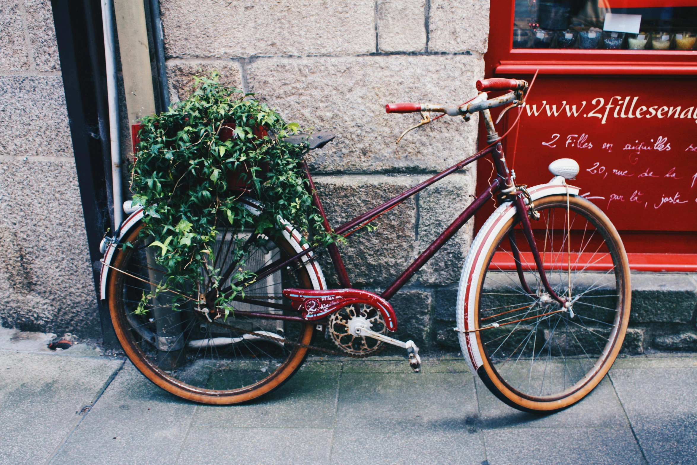 a red bicycle parked next to a building, by Nina Hamnett, pexels contest winner, art nouveau, lush greenery, scottish, maroon accents, upcycled