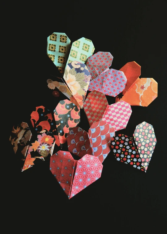 a pile of folded paper hearts on a black surface, sōsaku hanga, vibrant patterns, japanese collection product, sienna, lulu chen