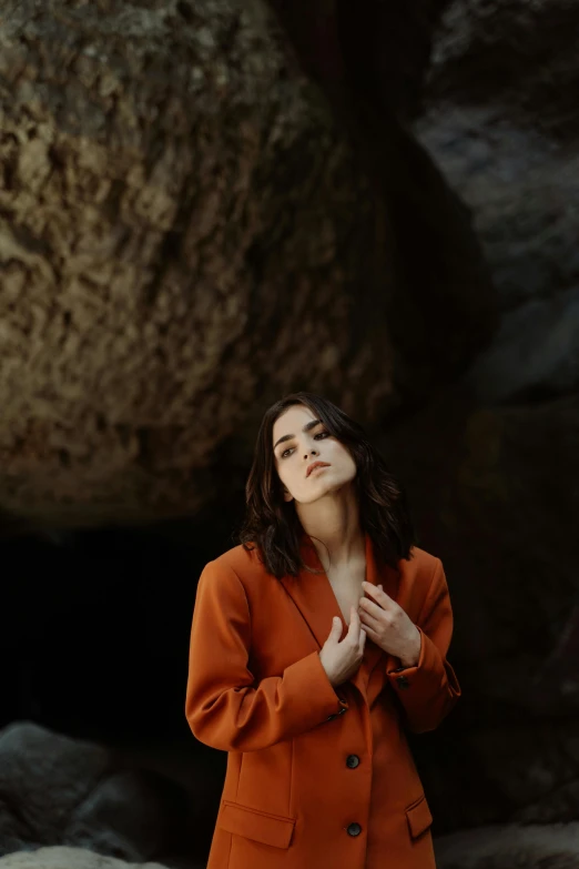 a woman standing in front of a large rock, orange jacket, sleek hands, charli bowater, classical