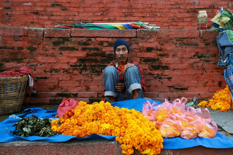 a man sitting in front of a pile of flowers, inspired by Steve McCurry, pexels contest winner, nepal, street market, avatar image, orange and blue colors