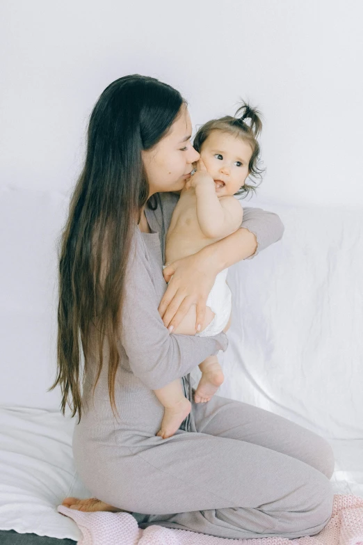 a woman sitting on a bed holding a baby, pexels, minimalism, wearing a baggy pajamas, light grey mist, profile image, mai anh tran