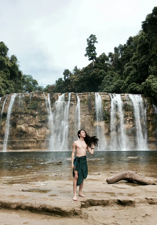 a man standing in front of a waterfall, an album cover, inspired by Lam Qua, pexels contest winner, sumatraism, bella poarch, no clothes, malaysian, highly upvoted