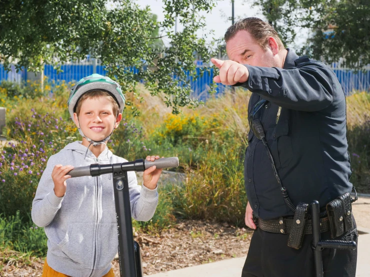 a man standing next to a boy on a scooter, wearing a police uniform, recreation, jc park, profile image