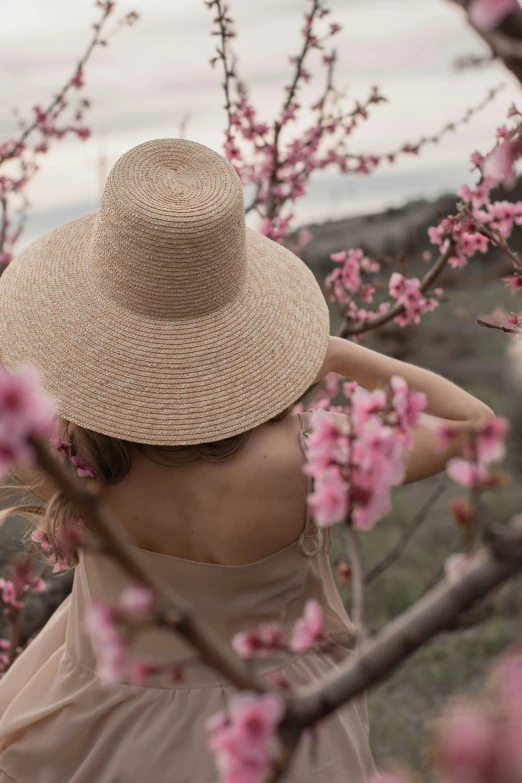 a woman in a hat standing next to a tree, unsplash contest winner, renaissance, spring flowers, bare back, with straw hat, peach