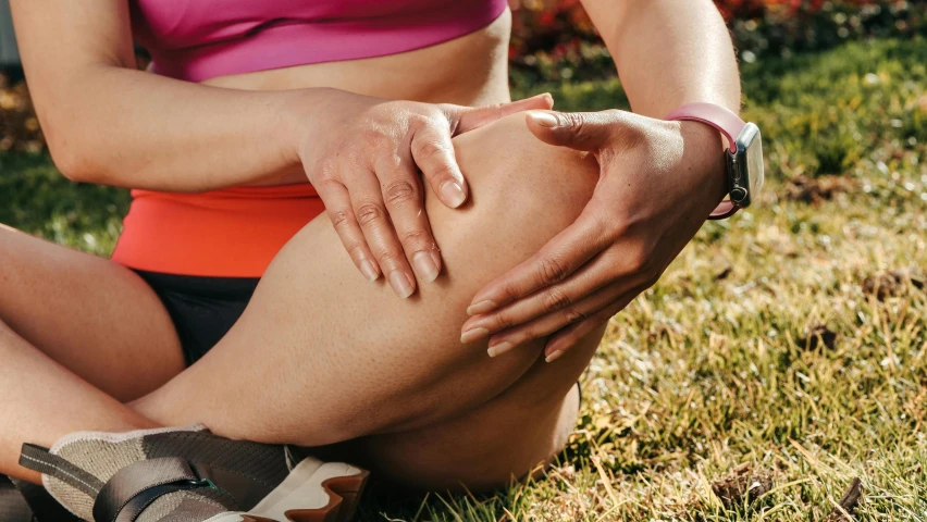 a woman sitting in the grass holding her knee, by Tom Bonson, trending on pexels, renaissance, swollen muscles, manuka, spa, caulfield