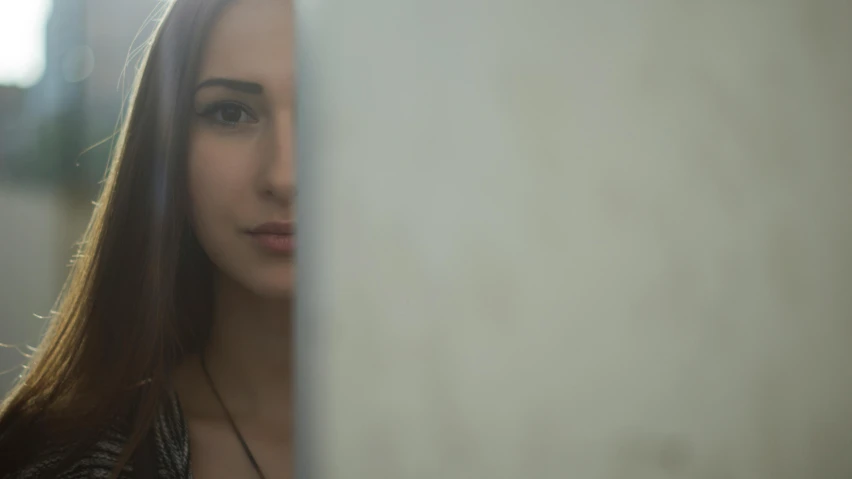 a beautiful young woman leaning against a wall, inspired by Elsa Bleda, pexels contest winner, photorealism, looking in mirror at older self, 4 k film still, in a claustrophobic, high angle closeup portrait