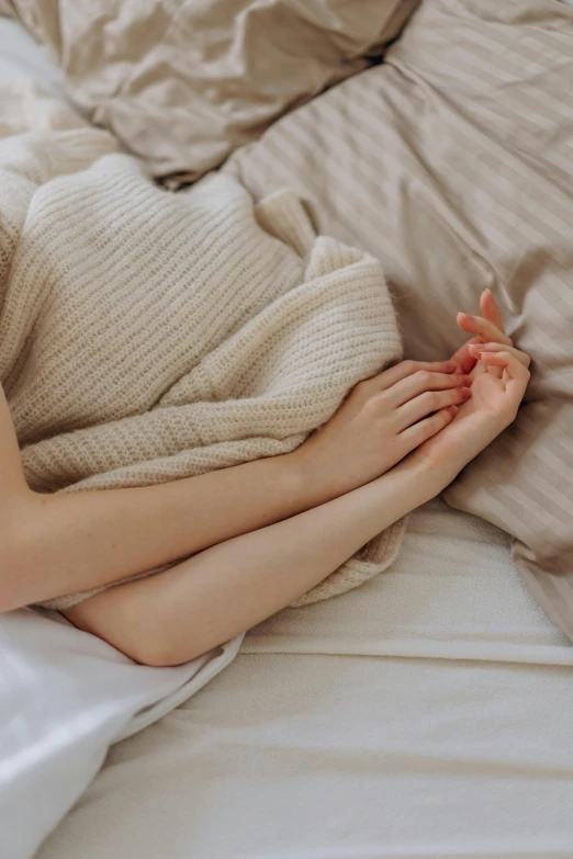 a woman laying on top of a bed covered in a blanket, inspired by Elsa Bleda, trending on pexels, romanticism, holding hands, smooth pale skin, sitting with wrists together, slightly pixelated