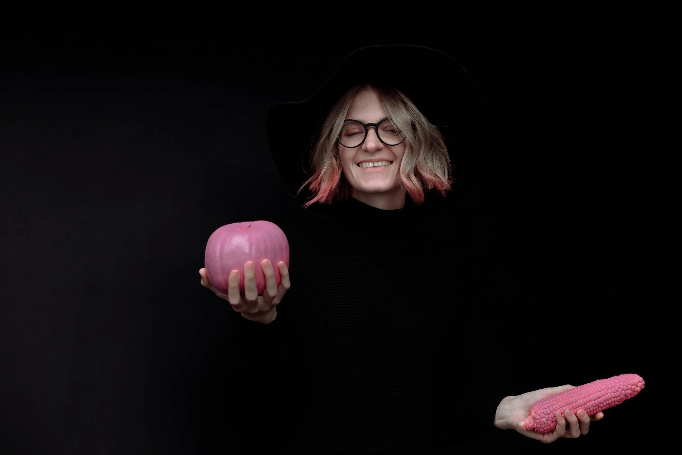a woman in a black hat and glasses holding a pink object in one hand and a pink object in the other, by Kristian Zahrtmann, pexels contest winner, she is a gourd, diablo 4 lilith, izombie, with apple