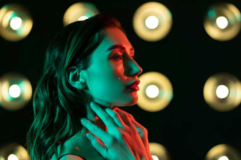 a woman standing in front of a wall of lights, a portrait, inspired by Elsa Bleda, trending on pexels, digital art, light makeup, red and green lighting, young woman looking up, with glow on some of its parts