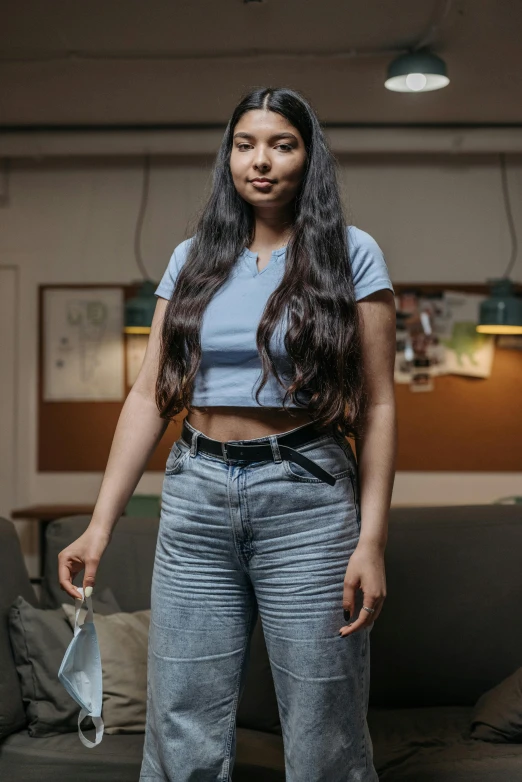 a woman standing in a living room next to a couch, by Adam Marczyński, pexels contest winner, hyperrealism, long wavy black hair, jeans and t shirt, in a classroom, wearing a crop top