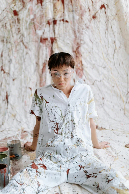 a boy sitting on the ground with paint all over him, an album cover, inspired by Shōzō Shimamoto, trending on unsplash, gutai group, a very macular woman in white, marble room, painted overalls, jingna zhang