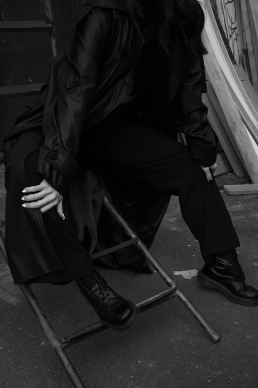 a black and white photo of a man sitting on a chair, an album cover, by Caro Niederer, unsplash, worn black coat, legs intertwined, photograph of a techwear woman, androgynous person