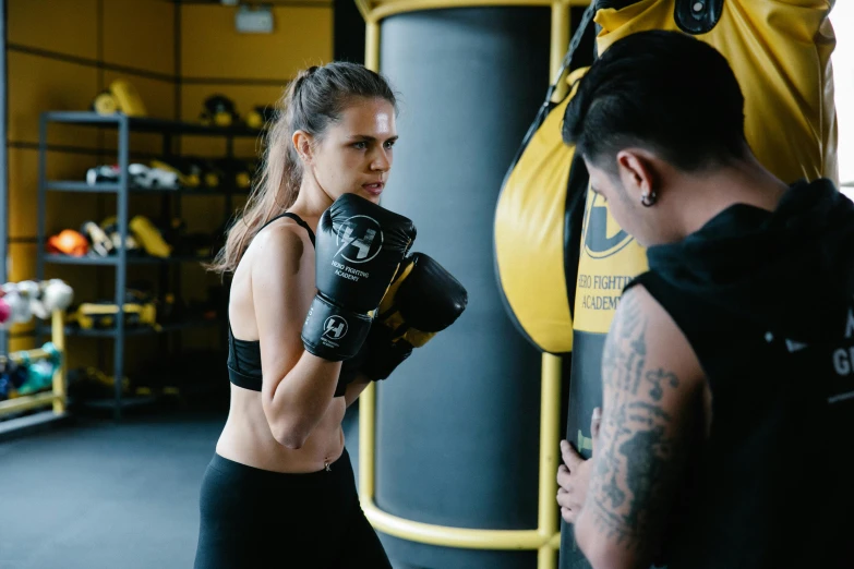 a woman standing in front of a punching bag, pexels contest winner, hurufiyya, black and yellow tracksuit, male and female, australian, grading