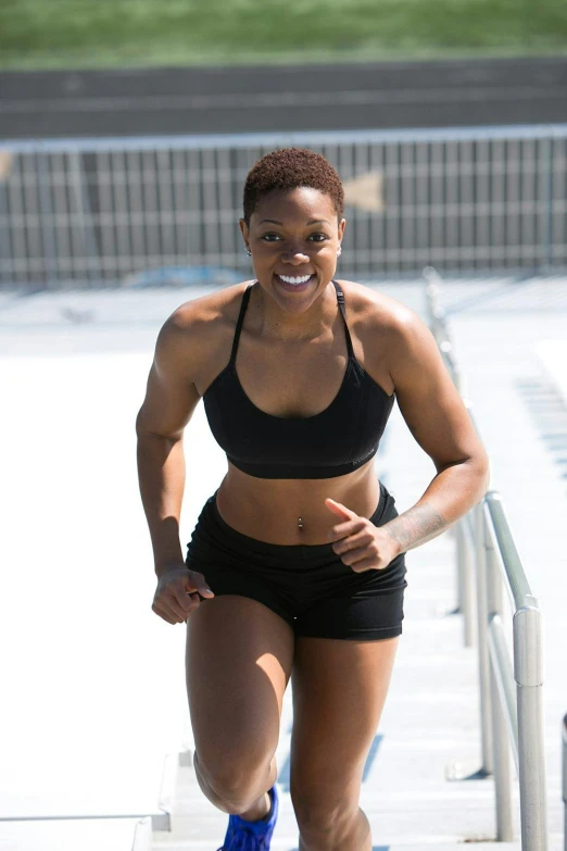 a woman running down a flight of stairs, wearing a cropped black tank top, dark skin tone, smiling, sport bra and shorts