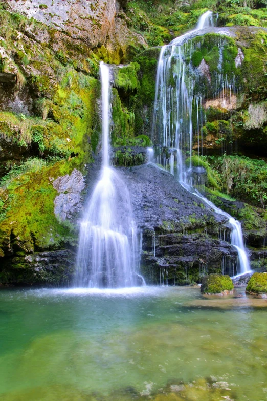 a waterfall in the middle of a lush green forest, deep clear pools of water, delightful surroundings, black forest, rock pools