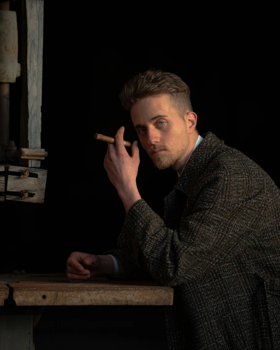 a man sitting at a table smoking a cigarette, a character portrait, inspired by Peter Rockwell, pexels contest winner, bauhaus, ryan gosling, androgynous person, holding a wood piece, standing with a black background