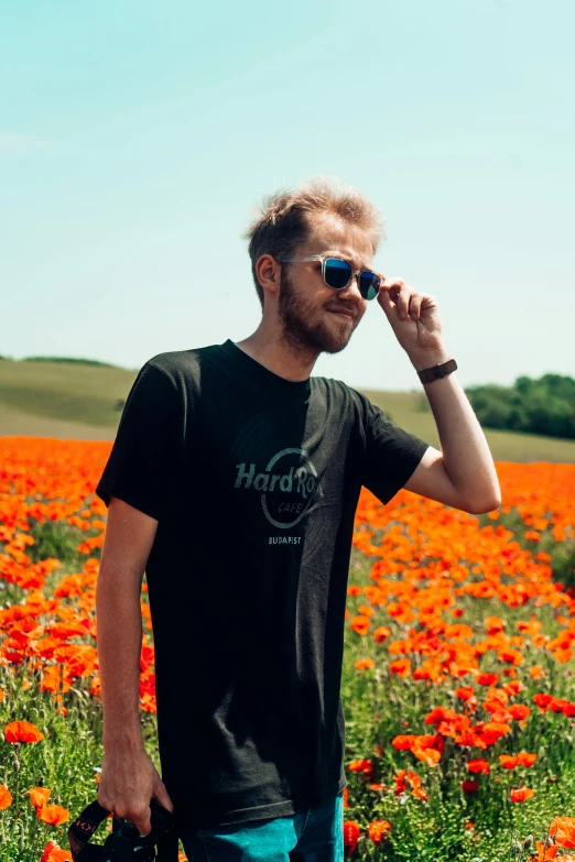 a man standing in a field of flowers talking on a cell phone, pexels contest winner, color field, wearing black tshirt, wearing shades, blonde british man, discord profile picture