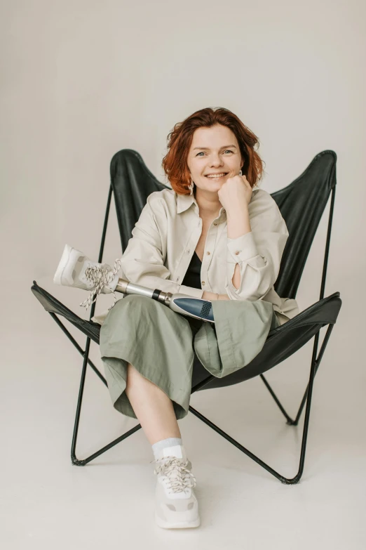 a woman sitting in a chair with her hand on her chin, an album cover, by Grytė Pintukaitė, pexels contest winner, with a walking cane, sadie sink, full body potrait holding bottle, relaxing and smiling at camera