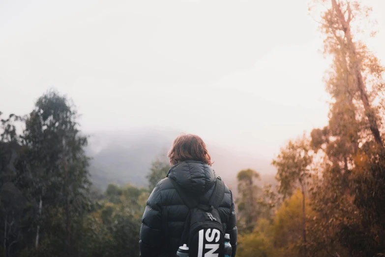 a person with a backpack walking down a dirt road, puffer jacket, portrait featured on unsplash, overlooking a valley with trees, profile picture 1024px