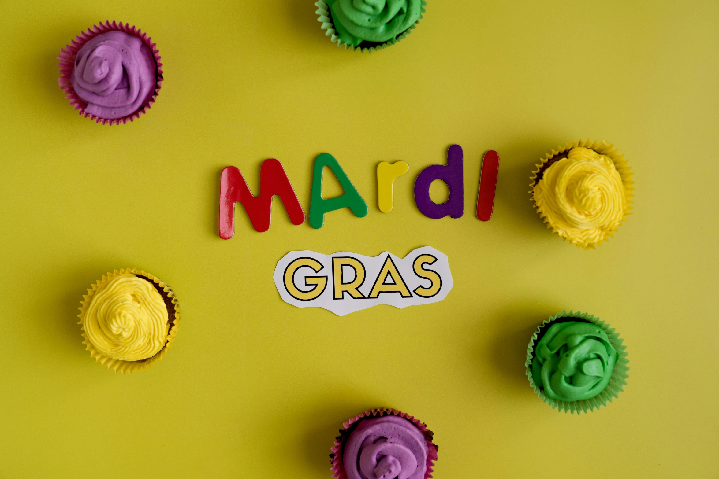 a group of cupcakes sitting on top of a yellow surface, inspired by Mardi Barrie, trending on pexels, graffiti, fake grass, word, new orleans, background image