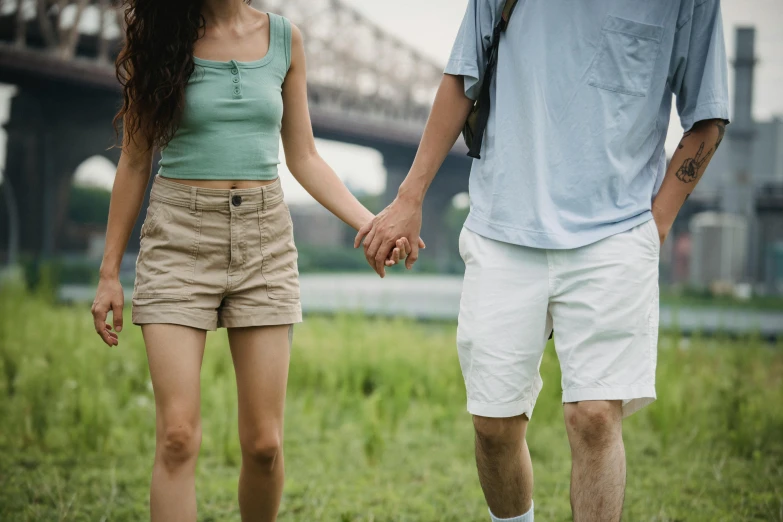 a man and a woman holding hands in a field, a colorized photo, trending on pexels, in shorts, bridges, in a city park, hand holding cap brim