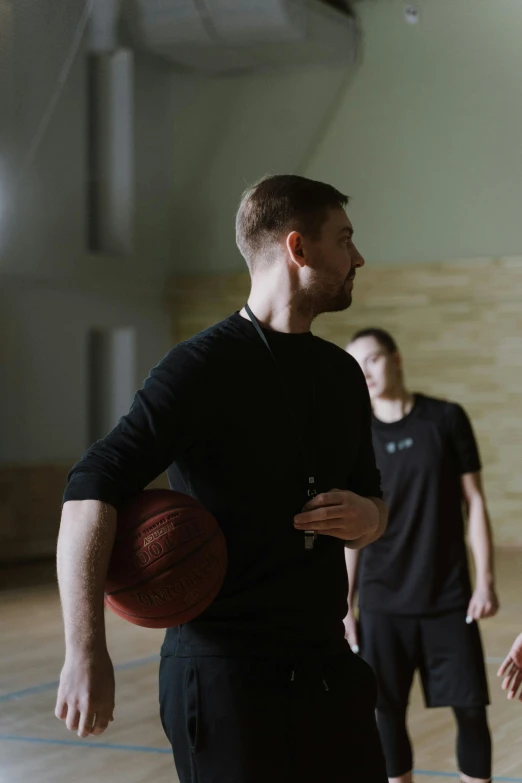 a group of men standing on top of a basketball court, a picture, by Adam Marczyński, holding a ball, man in black, b - roll, teaching
