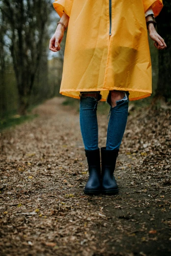 a woman in a yellow raincoat standing on a path, pexels, jeans and black boots, laura watson, in the wood, festivals