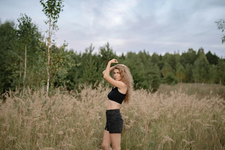 a woman standing in a field of tall grass, inspired by Elsa Bleda, unsplash, tight black tank top and shorts, russian girlfriend, wavy hair spread out, 15081959 21121991 01012000 4k