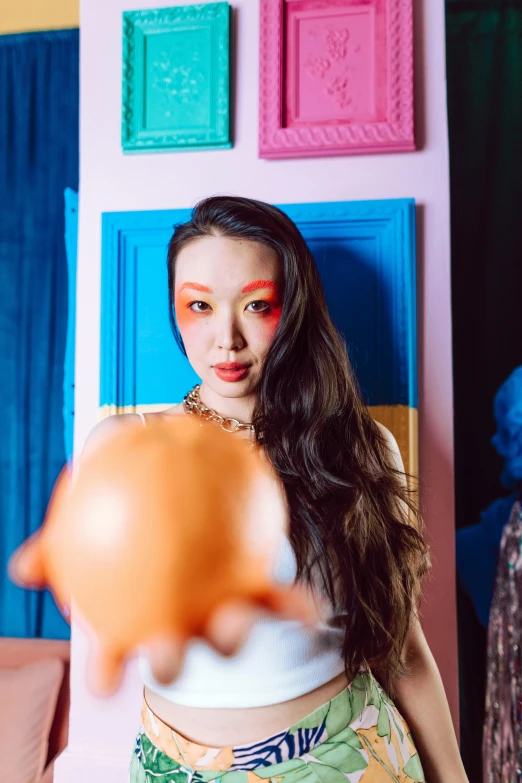 a woman holding an orange in front of her face, an album cover, by Julia Pishtar, unsplash, pop surrealism, david choe, jaeyeon nam, looking directly at the camera, toys