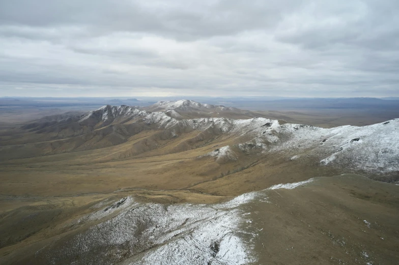 a person standing on top of a snow covered mountain, hurufiyya, an expansive grassy plain, drone photograph, rocky hills, distant photo