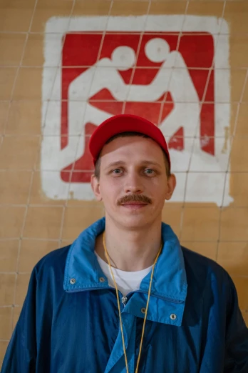 a man standing in front of a red and white sign, an album cover, inspired by Graham Forsythe, featured on reddit, graffiti, thin moustache, russian academic, headshot portrait, red cap