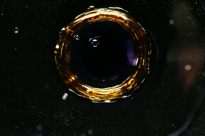 a glass filled with liquid sitting on top of a table, by Otto Piene, space art, gold gilded circle halo, taken through a telescope, galactic dark colors, honey