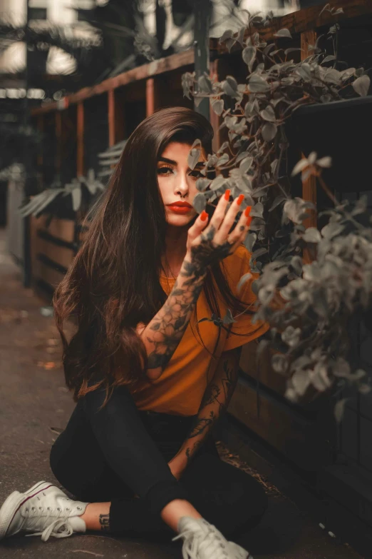 a woman sitting on the ground in front of a fence, a tattoo, inspired by Elsa Bleda, trending on pexels, 👅 👅, young woman with long dark hair, hands on face, tattoo parlor photo