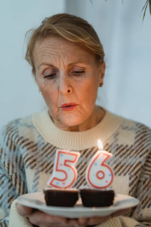 a woman holding a plate with two cupcakes on it, an album cover, inspired by Cornelia Parker, pexels contest winner, portrait 6 0 - year - old woman, candle lightning, 9 5, alec soth : : love