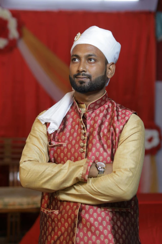 a man in a red and gold outfit standing with his arms crossed, inspired by Manjit Bawa, hurufiyya, he is in a mosque, post graduate, slightly pixelated, groom